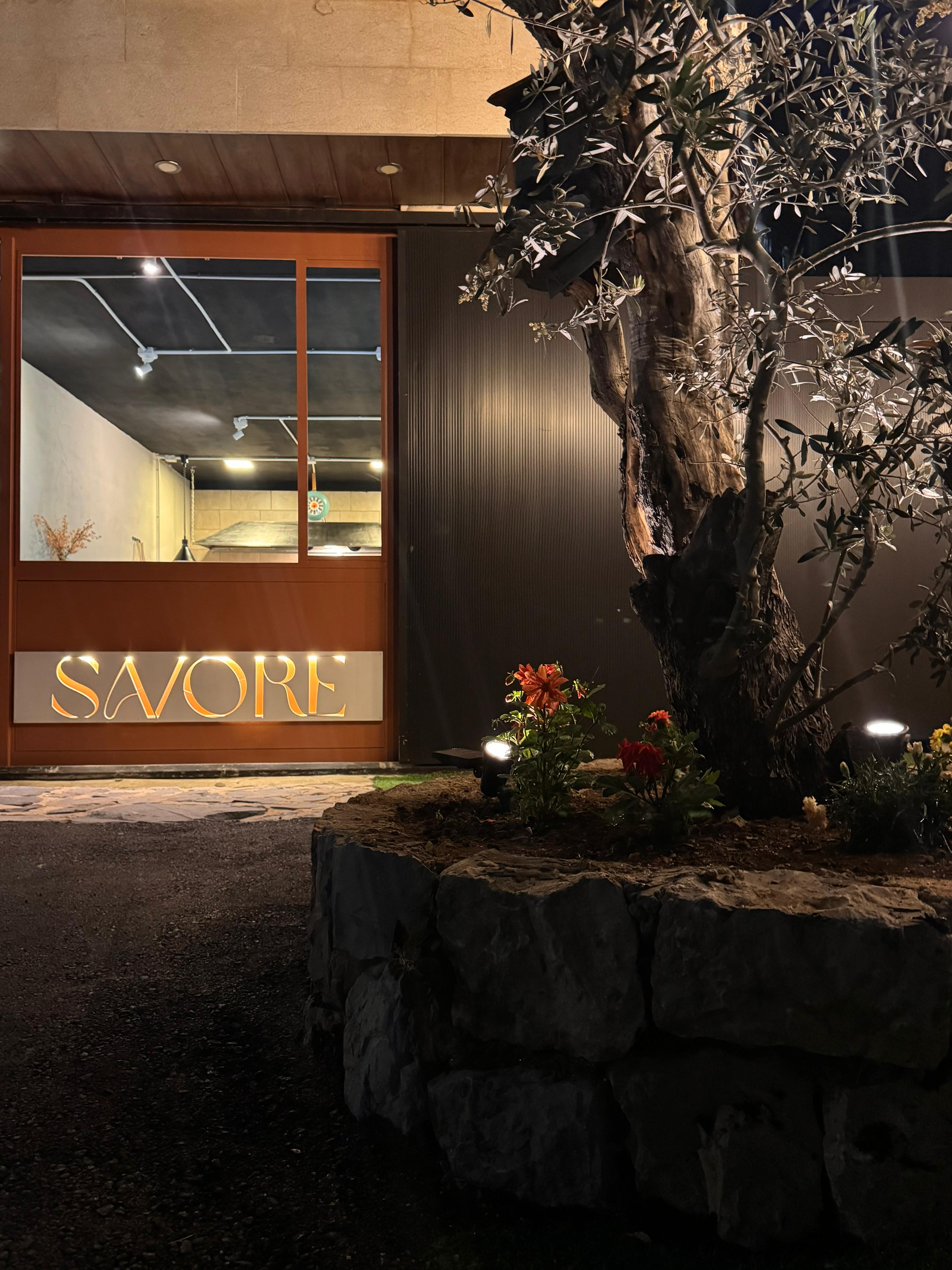 Savore's illuminated storefront at night with an olive tree in the mountains of Lebanon