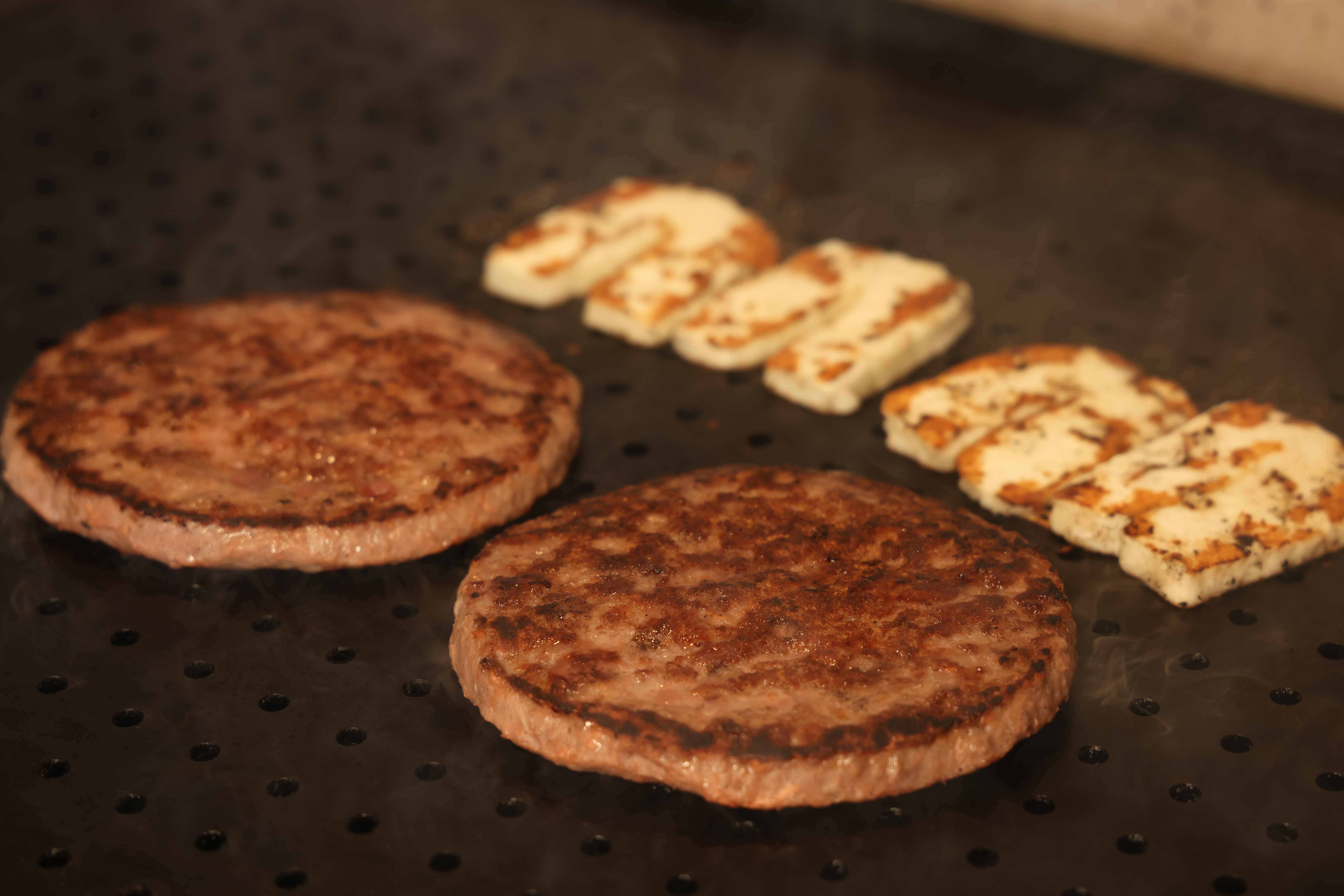 Beef patties and grilled halloumi searing on a hot flat-top griddle
